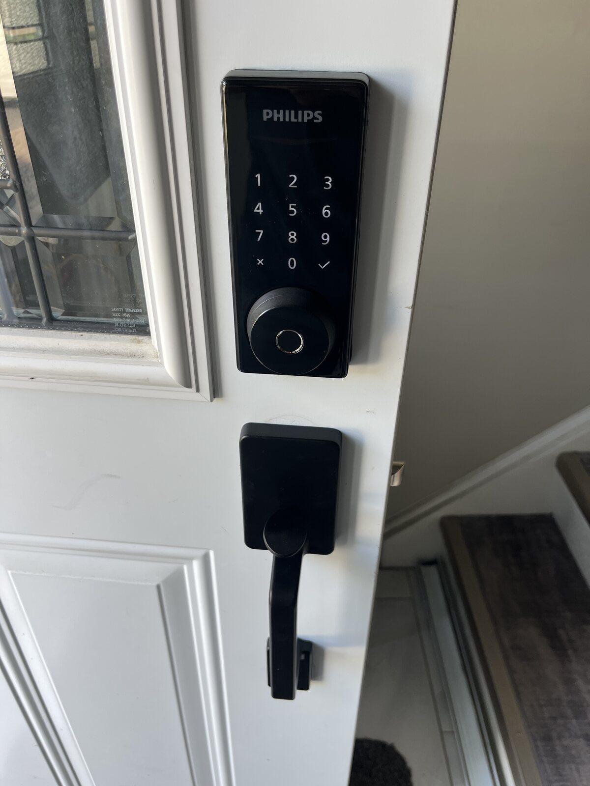 Black Philips fingerprint keypad deadbolt and matching lever handle installed on a white residential entry door in Orleans