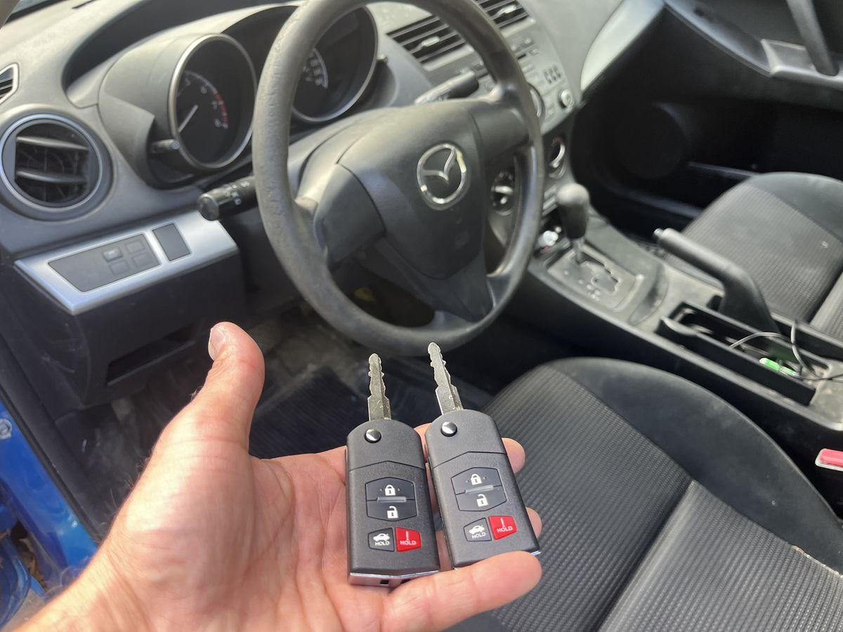 Two duplicated car key fobs held next to a vehicle's steering wheel
